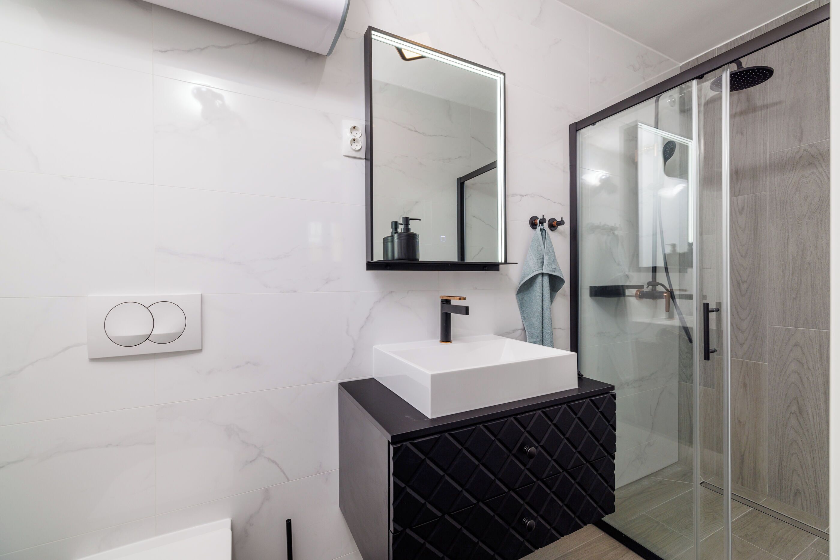 Un bagno moderno con un lavandino bianco, un mobile contenitore nero e un box doccia in vetro.
