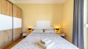 Een slaapkamer met een bed, nachtkastjes, een kledingkast en een nachttafeltje met lampen.