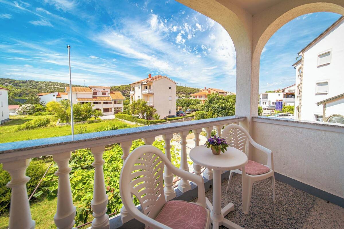 A balcony with a table and chairs, overlooking a residential area with houses and greenery.