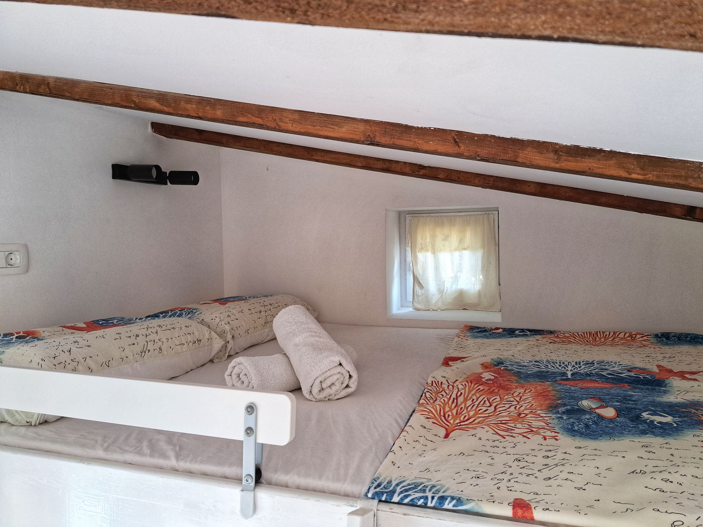 A small, cozy room with a bunk bed, a small window with a curtain, and a wall socket.