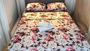 Ein Bett mit blumigem Bettzeug, zwei Kissen und ein zusammengerolltes Handtuch.