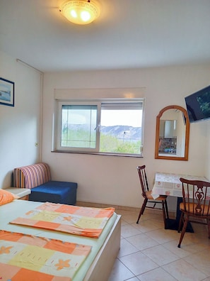 Un dormitorio con cama, escritorio, silla, ventana que ofrece vistas a colinas y una lámpara en el techo.
