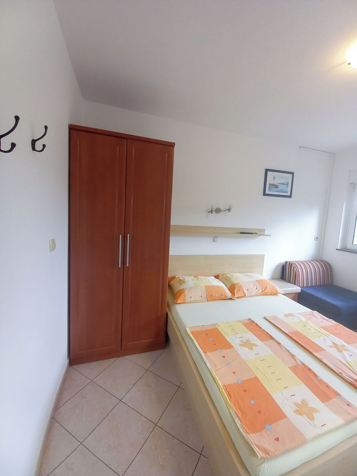 A bedroom with a bed, a wardrobe, a bedside table, and a window.