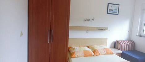 A bedroom with a bed, a wardrobe, a bedside table, and a window.