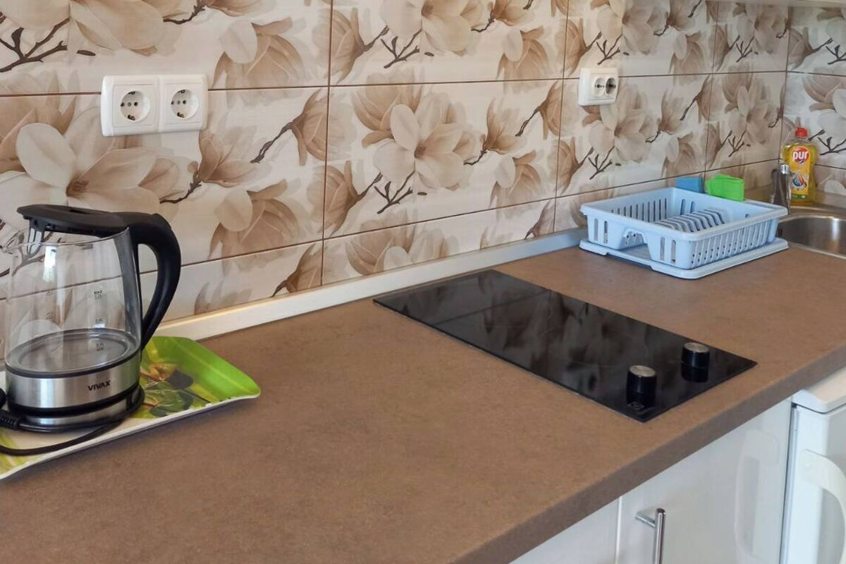 A kitchen with a countertop, a kettle, a dish rack, and a window above the sink.