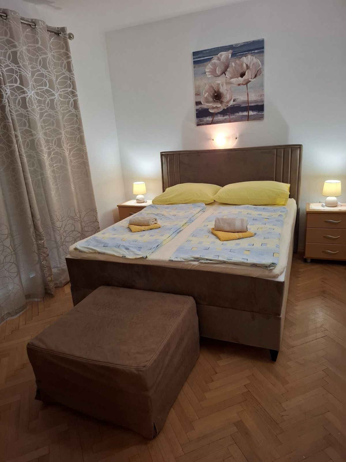 Een slaapkamer met een bed, twee nachtkastjes, een bankje en een schilderij aan de muur.