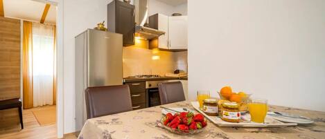 A dining area with a table set for two, a bowl of strawberries, a glass of orange juice, and a jar of jam.