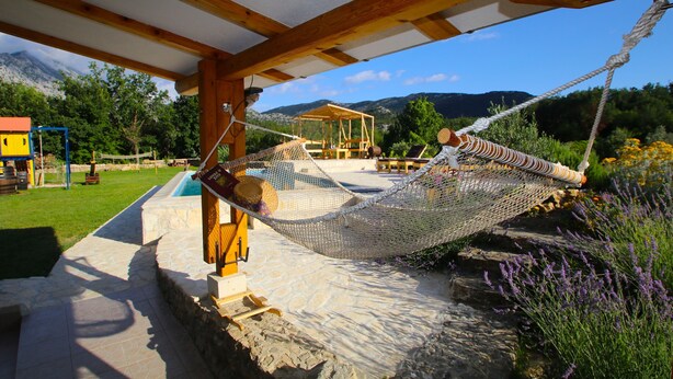 Eine Hängematte unter einer Holzpergola, ein Steinweg und ein Blick auf eine gebirgige Landschaft.