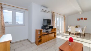 Ein geräumiger Wohnbereich mit einer Holz-Unterhaltungseinheit, einem Fernseher, einem Esstisch mit Stühlen und Blick durch ein großes Fenster.