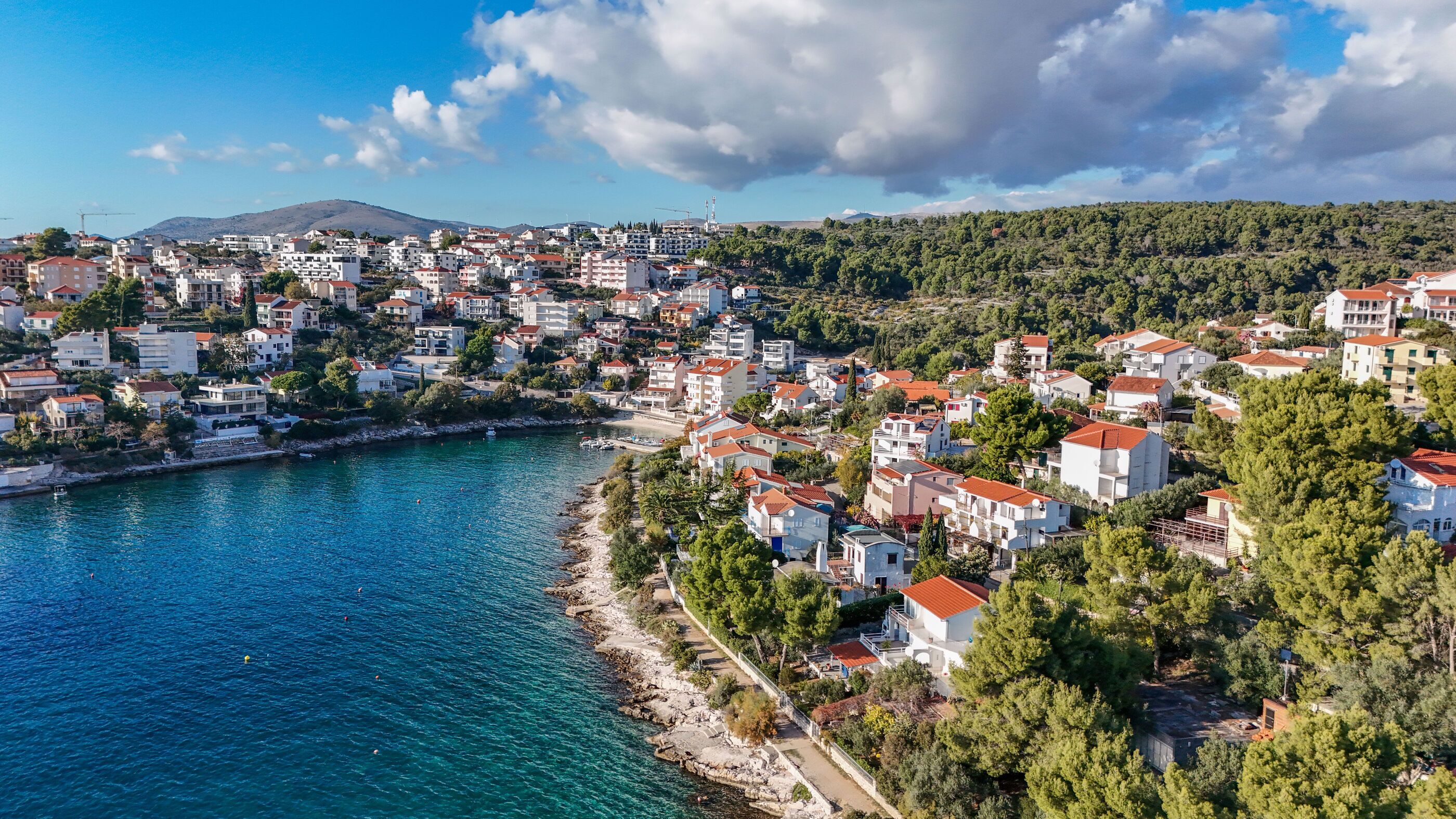 A coastal town with buildings along the waterfront, a clear sky, and a hilly backdrop.