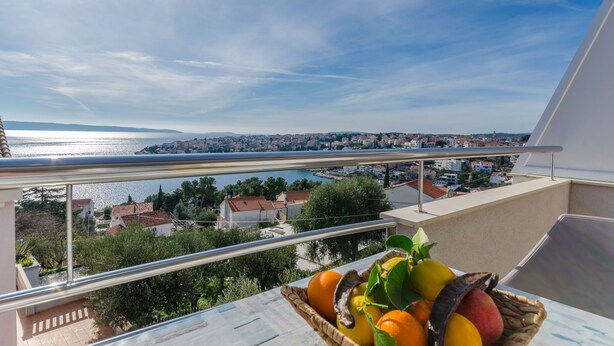 Ein Balkon mit Blick auf eine Küstenstadt, eine Obstkorb und ein klarer Himmel.