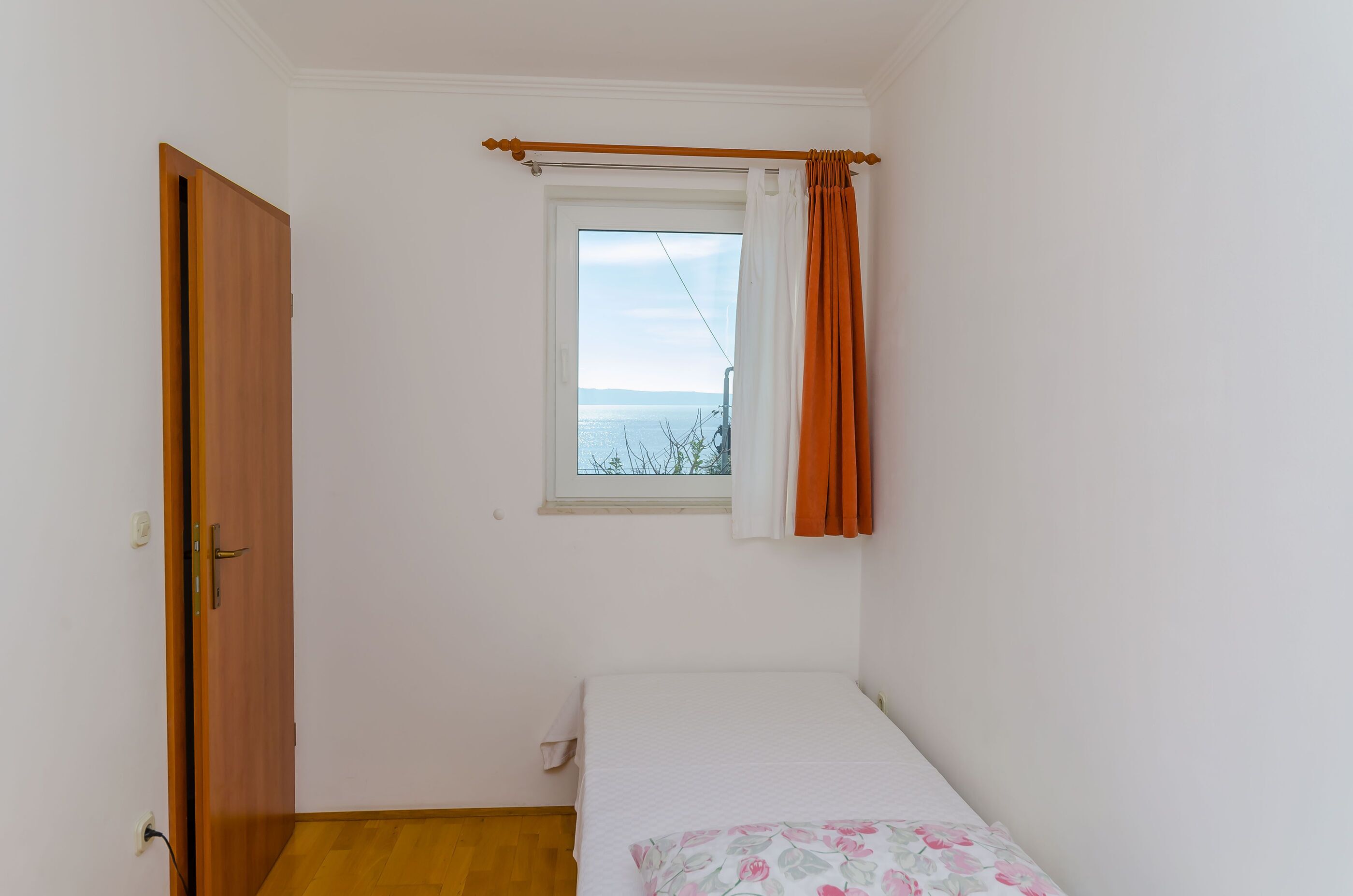 A small bedroom with a single bed, a window with curtains, and a door.