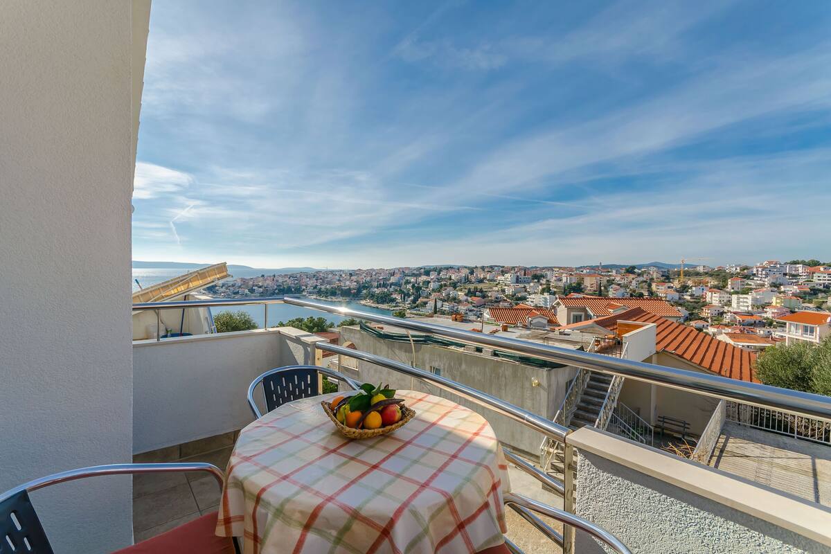 Un balcon avec une table et des chaises, un saladier rempli de fruits et une vue sur la ville.