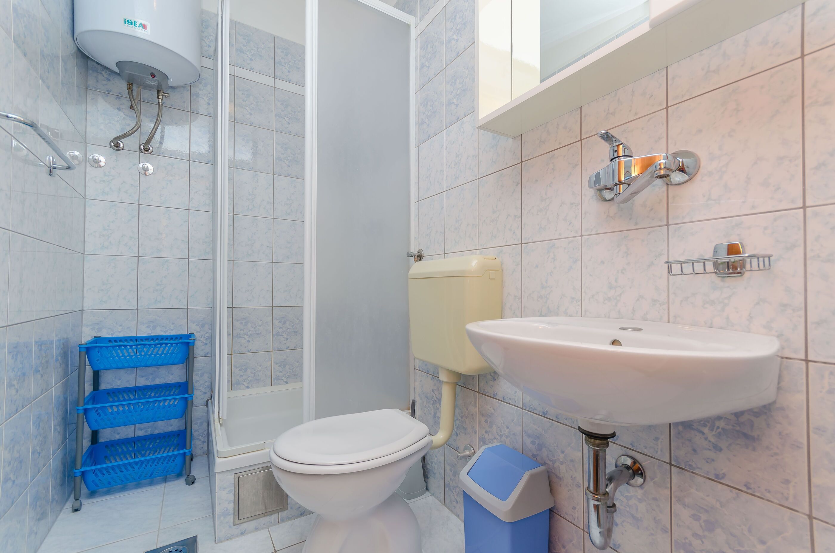 A bathroom with a toilet, sink, shower, and blue storage baskets.