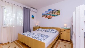 A bedroom with a wooden bed, a nightstand, a small cabinet, and a wall with a landscape painting. - Apartments KK (Omis)