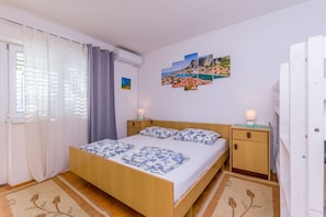 A bedroom with a wooden bed, a nightstand, a small cabinet, and a wall with a landscape painting. - Apartments KK (Omis)