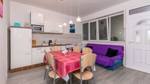 A compact kitchen with white cabinets, a microwave, and a dining table set with chairs. - Apartments KK (Omis)