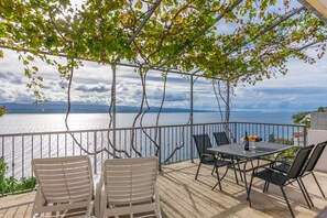 An outdoor terrace with a table and chairs, overlooking a body of water and a mountainous landscape. - Apartments KK (Omis)