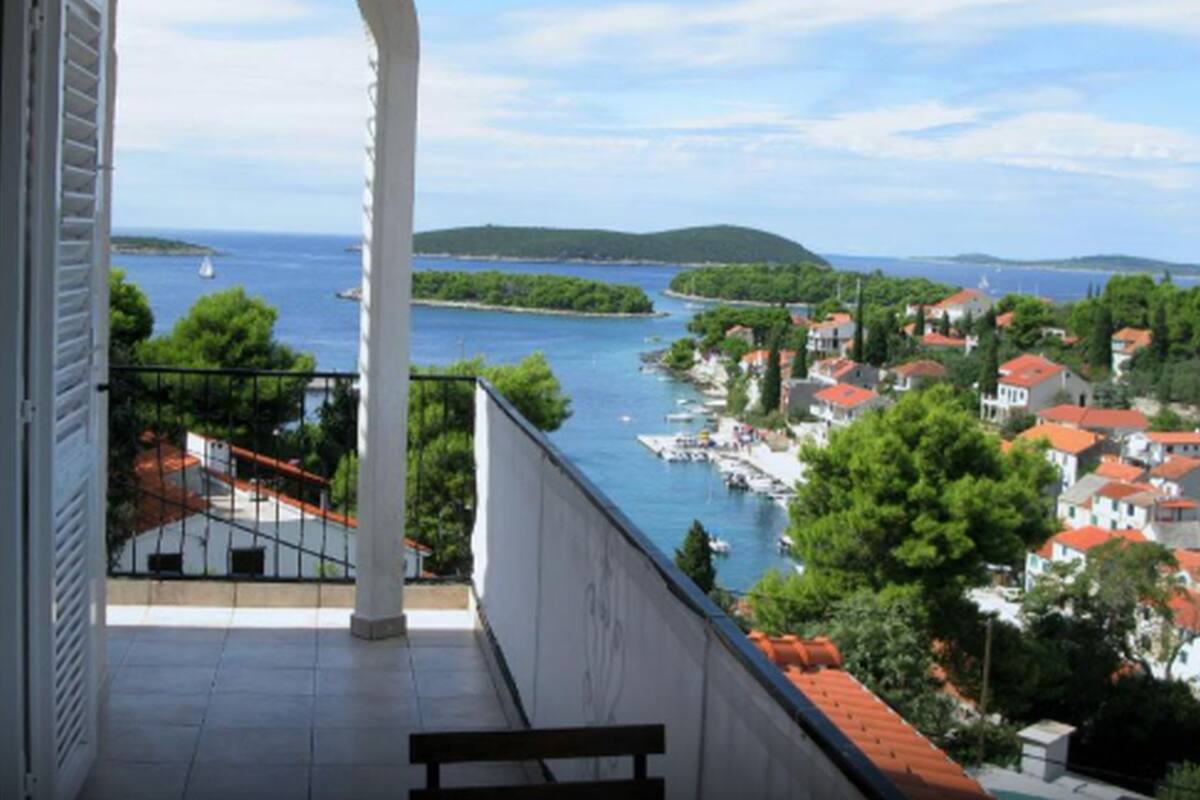 Un balcon donnant sur une ville côtière, avec un ciel dégagé et une étendue d’eau.
