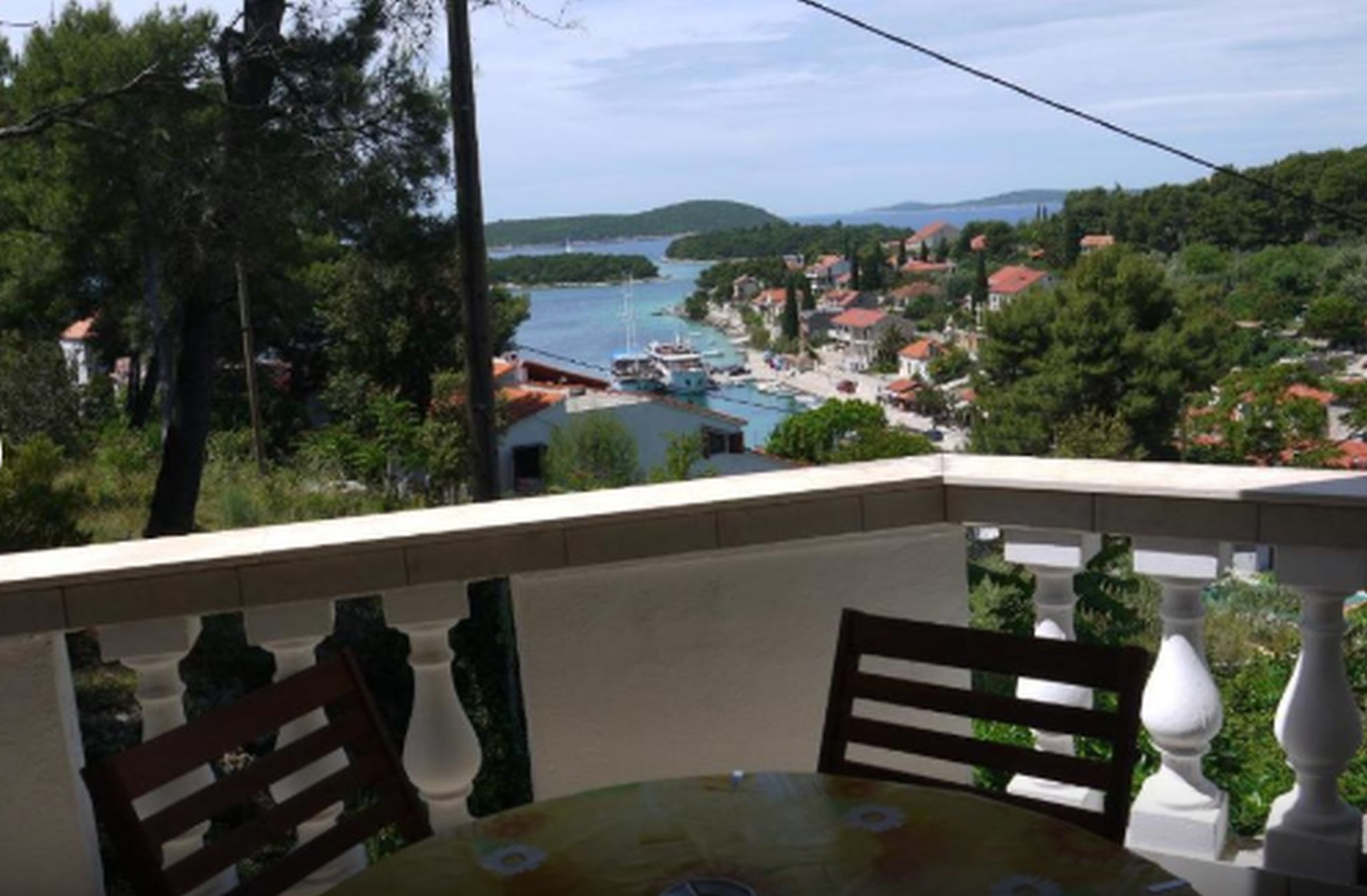 Een balkon met een tafel en stoelen met uitzicht op een kustplaatsje met boten en huizen.