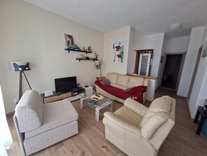 Un salon comprenant un canapé, un fauteuil, une table basse, un téléviseur et un lampadaire.