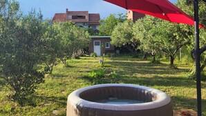A hot tub in a garden with a red umbrella, surrounded by greenery and a house in the background. - House Garden House (Kastela)