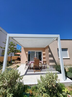 Un patio couvert avec une table et des chaises, une plante en pot et une vue sur un bâtiment doté d’une fenêtre.