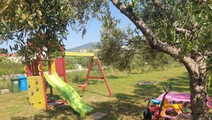 A playground with a slide, swings, and a small table under a tree. - House Garden House (Kastela)