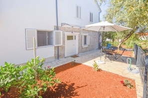 A courtyard with a white building, a door, and a table with an umbrella. - Apartments Toni (Preko)