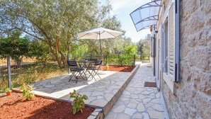An outdoor patio area with stone flooring, a table and chairs, and an umbrella. - Apartments Toni (Preko)