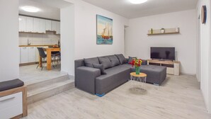 A modern living room with a grey sofa, a small round table with a vase, a flat-screen TV, and a painting of a sailboat on the wall. - Apartments Toni (Preko)