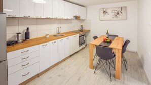 A modern kitchen with white cabinets, a wooden countertop, and a dining area with a table and chairs. - Apartments Toni (Preko)