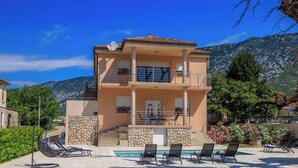 A two-story building with a pool area, outdoor seating, and a view of mountains. - Apartments Margita 2 (Vinodol)