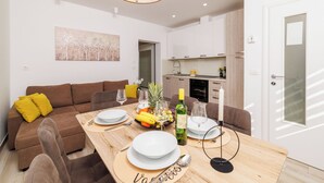 A modern living room with a dining table set for two, a sofa with yellow cushions, a kitchen in the background, and a ceiling fan. - Apartments Margita 2 (Vinodol)