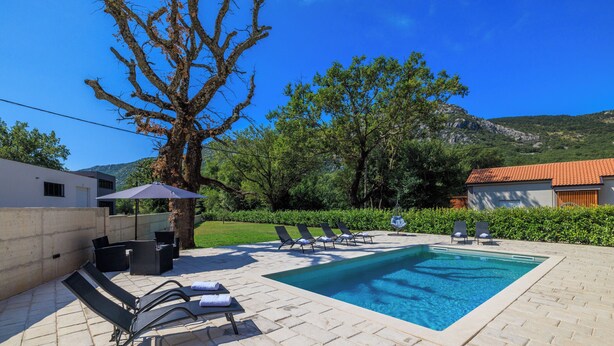A swimming pool area with lounge chairs and a table, surrounded by greenery and a mountain backdrop. - Apartments Margita 2 (Vinodol)