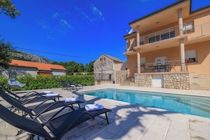 A swimming pool with lounge chairs and a stone building with a balcony. - Apartments Margita 2 (Vinodol)