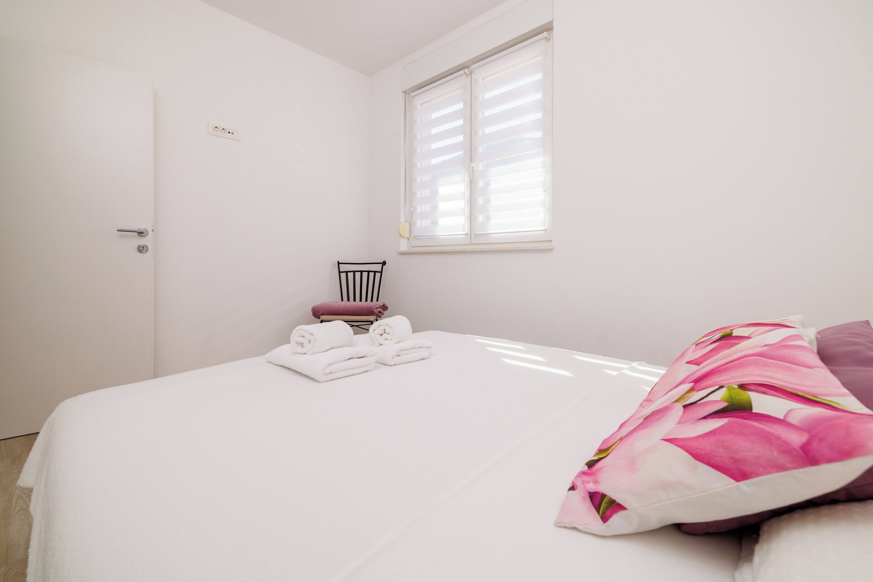 A bedroom with a bed, a chair, a window, and a door.