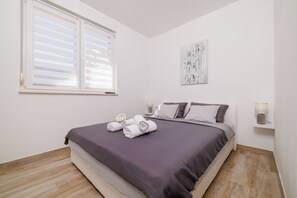 Une chambre à coucher avec un lit, des oreillers, une table de chevet avec une lampe et une fenêtre avec des stores.