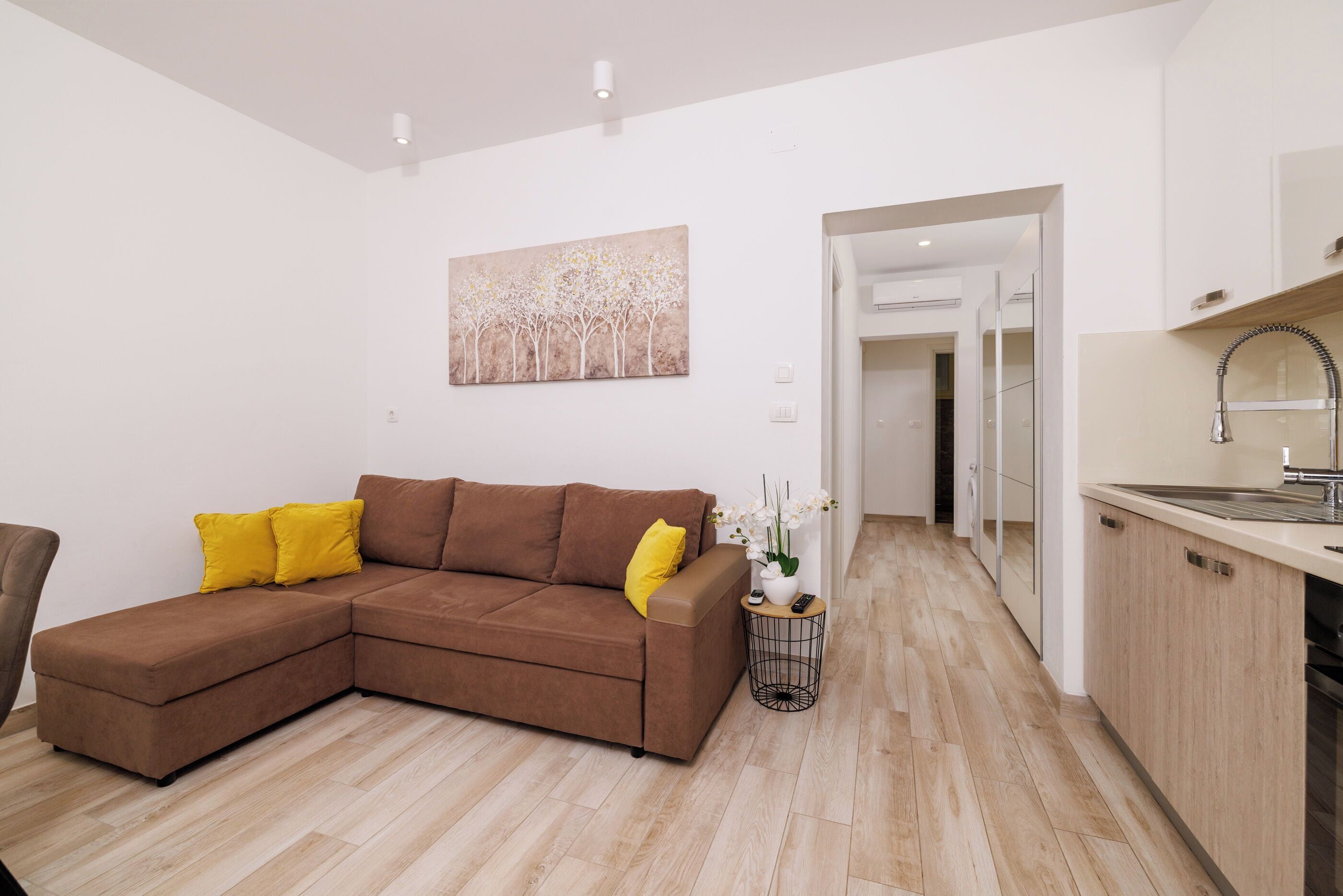 A modern living room with a brown sectional sofa, a small side table with a plant, and a painting on the wall.