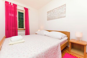 A bedroom with a bed, a nightstand, a lamp, a window with curtains, and a wall-mounted artwork. - Apartments La Mer (Pasman)