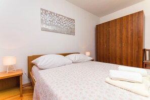 A bedroom with a wooden bed, white pillows, a bedside lamp, a wooden wardrobe, and a wall-mounted abstract painting. - Apartments La Mer (Pasman)
