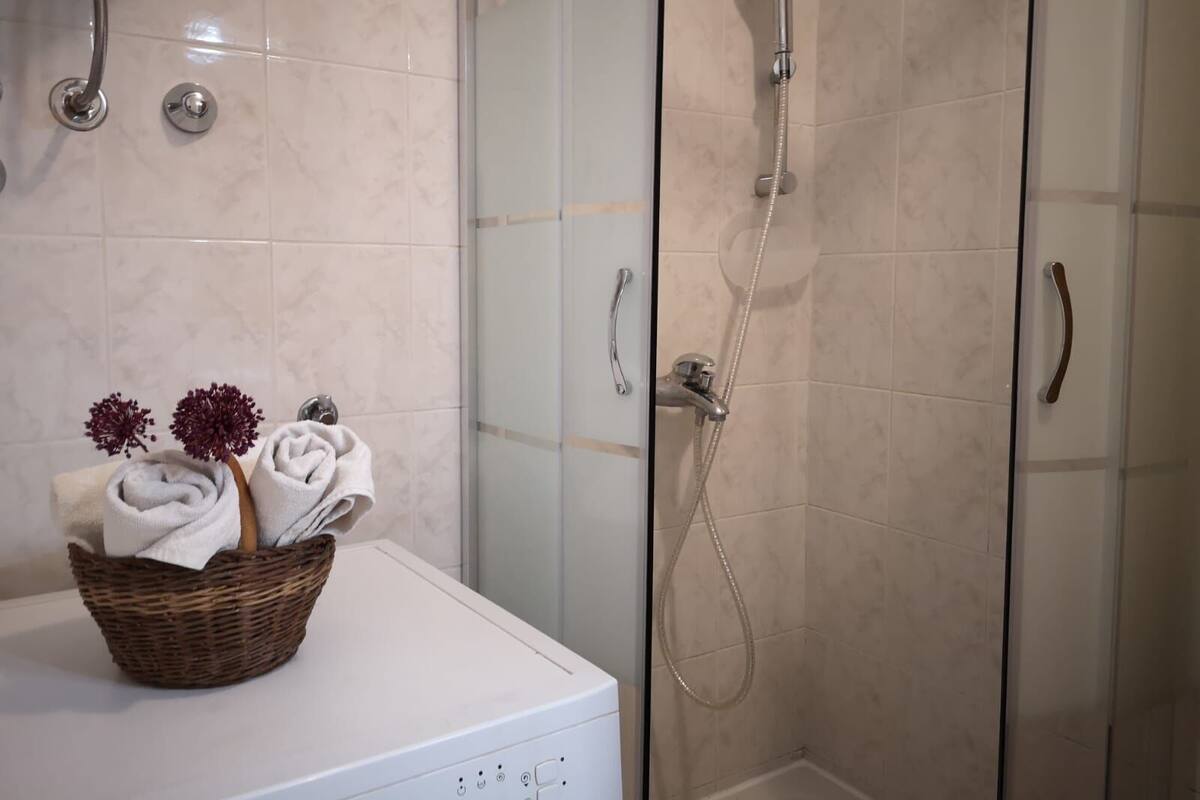 A bathroom with a glass shower enclosure, a white sink with a basket of towels, and a showerhead.