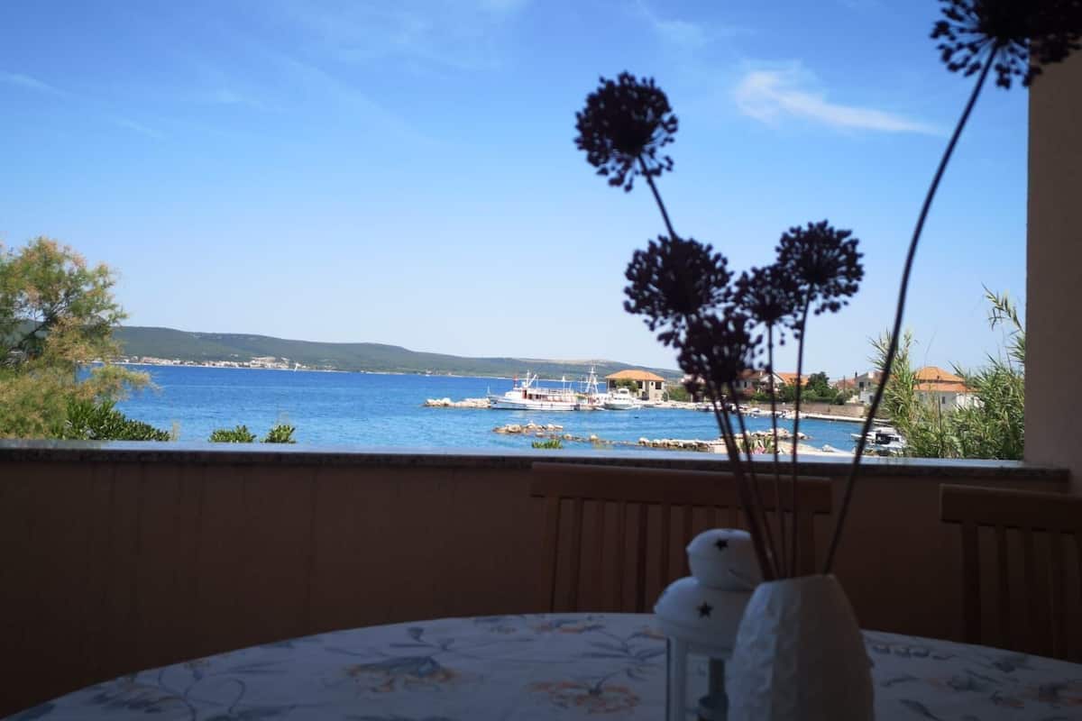 A balcony with a view of the sea, a table with a floral tablecloth, and decorative vases.