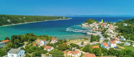 An aerial view of a coastal town with houses, a marina, and a clear blue sea.