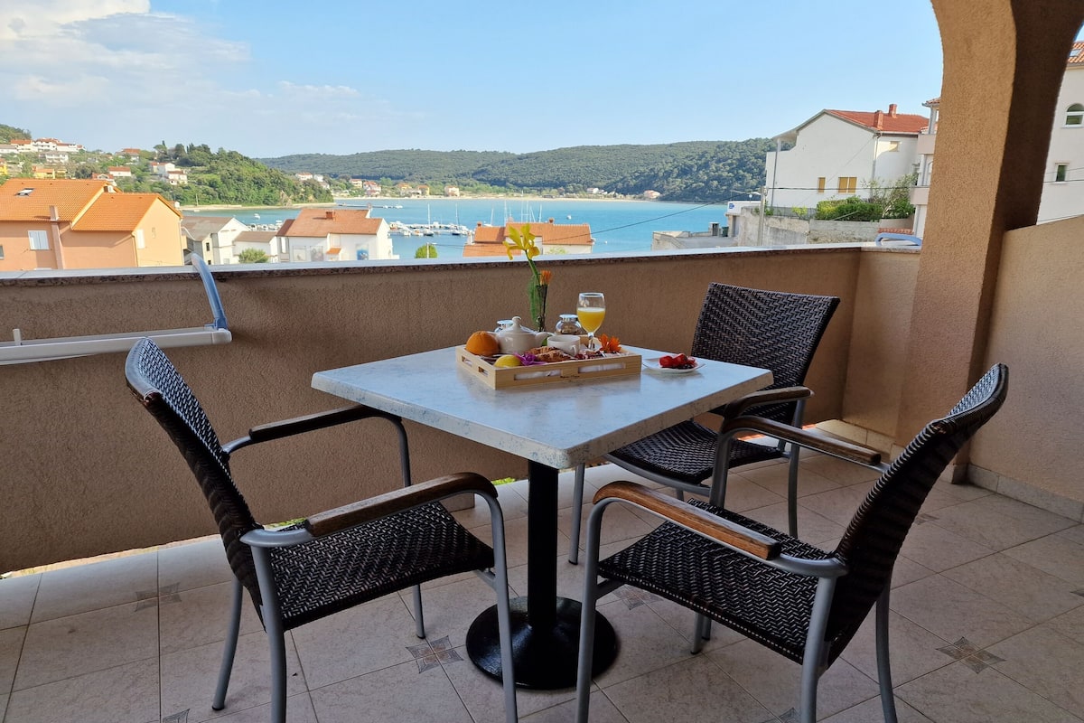A balcony with a table set for breakfast, overlooking a coastal view.