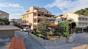 A residential area with a two-story building, a stone retaining wall with plants, and a paved road. - Apartment and Rooms Zora (Rab)