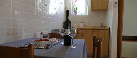 Een keuken met een eettafel gedekt voor twee personen, een fles wijn en een schaal fruit.