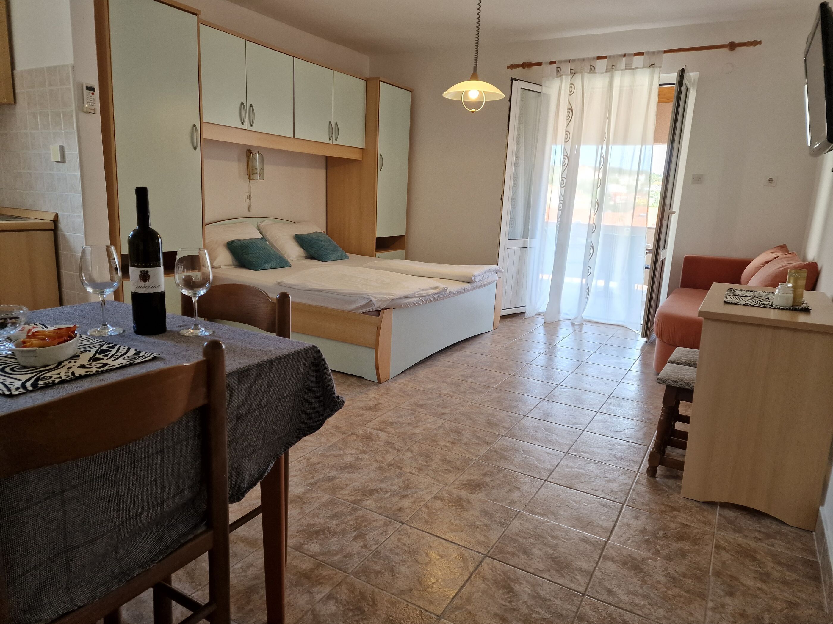 A compact room with a bed, a dining area with a table and chairs, a kitchenette, and a small seating area with a sofa.