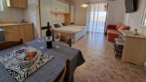 A compact living space with a kitchenette, a dining area with a table set for two, a bed, and a sofa. - Apartment and Rooms Zora (Rab)