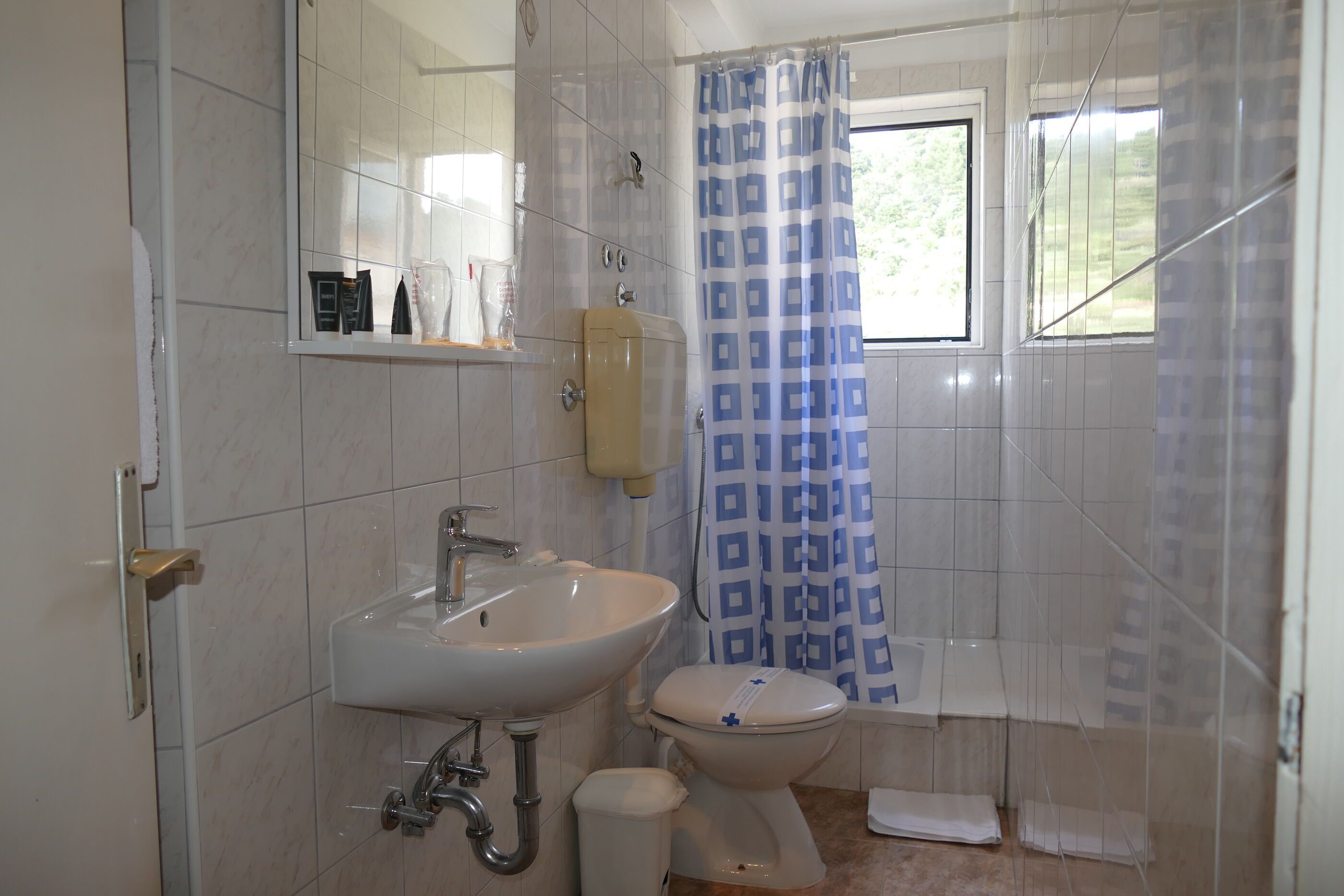 A bathroom with a sink, toilet, and a window with a shower curtain.